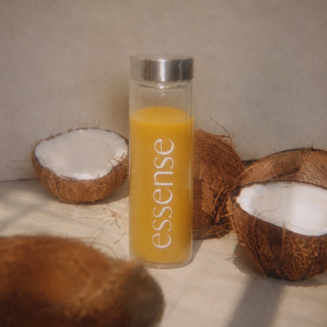 Essense glass water bottle filled with mixed Protocol 01 beside fresh coconut halves · coconut flavour daily longevity formula